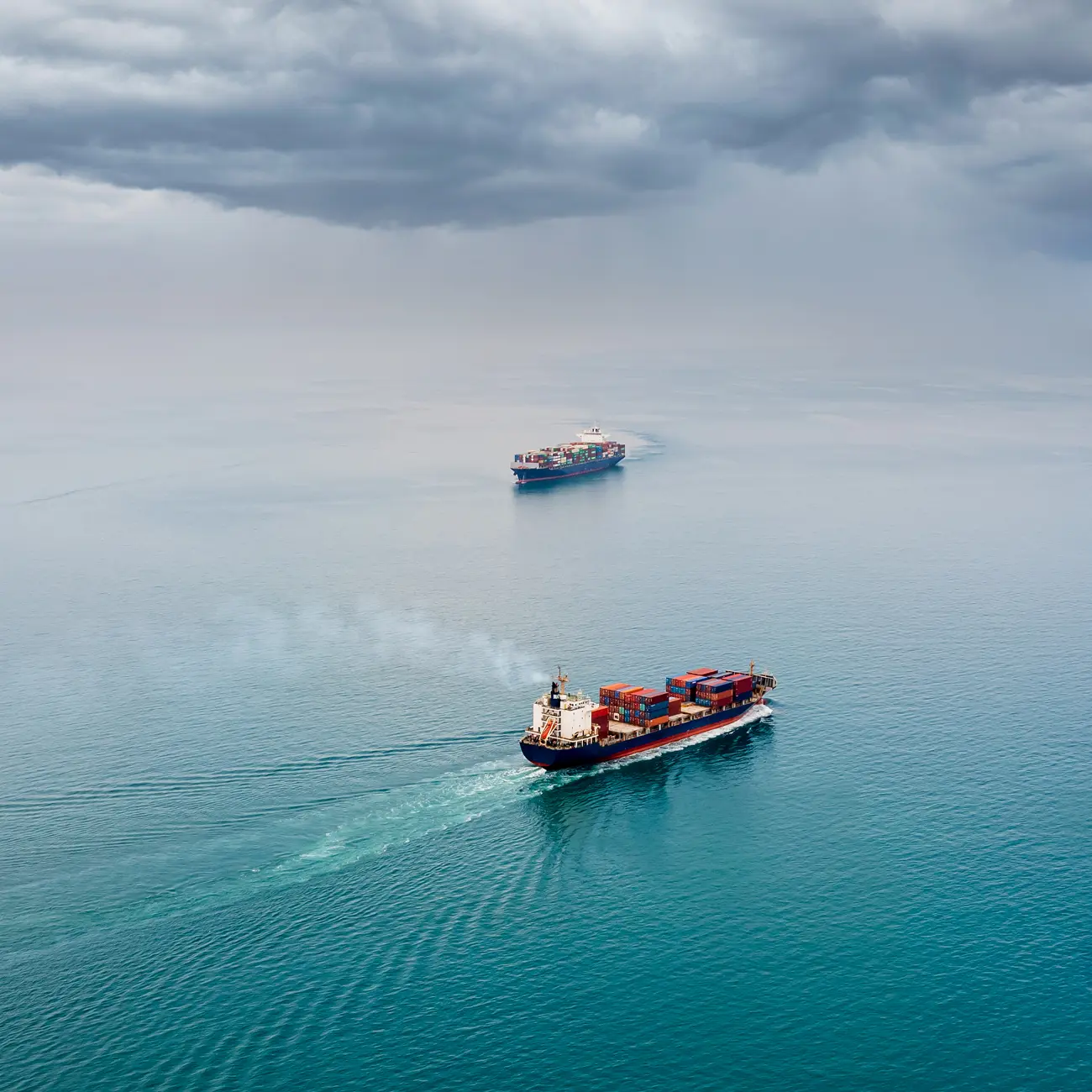 Two container cargo ships traveling across open ocean.