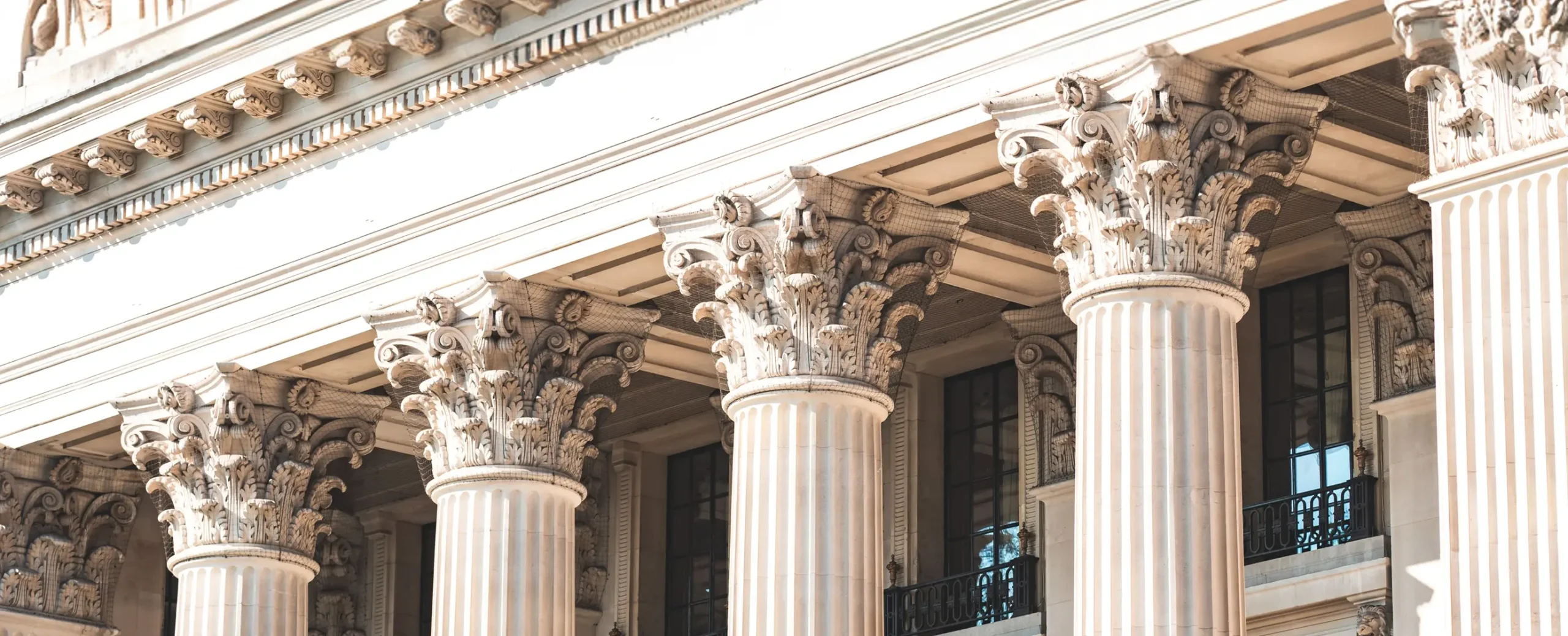 Ornate row of Corinthian columns with detailed capitals on a sunlit neoclassical building facade, evoking grandeur and elegance.