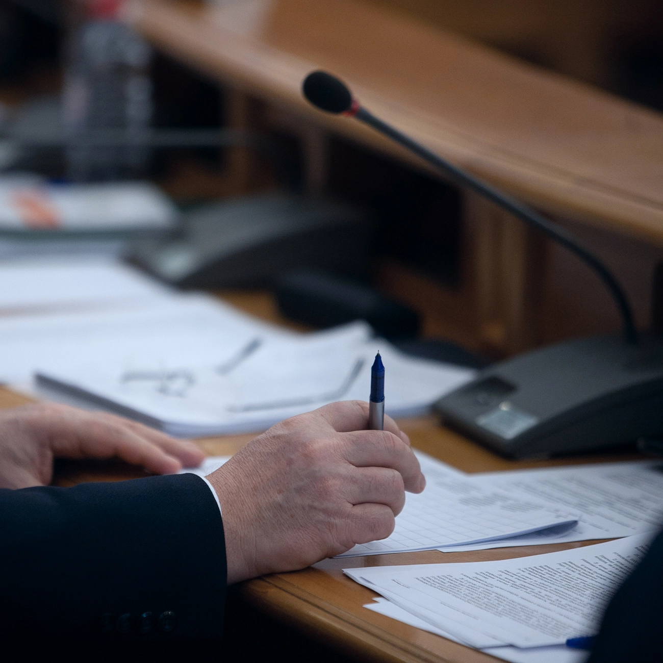 Person writing notes at a conference table with microphone.